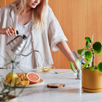 Woman watering a plant in a kitchen with a wooden wall background