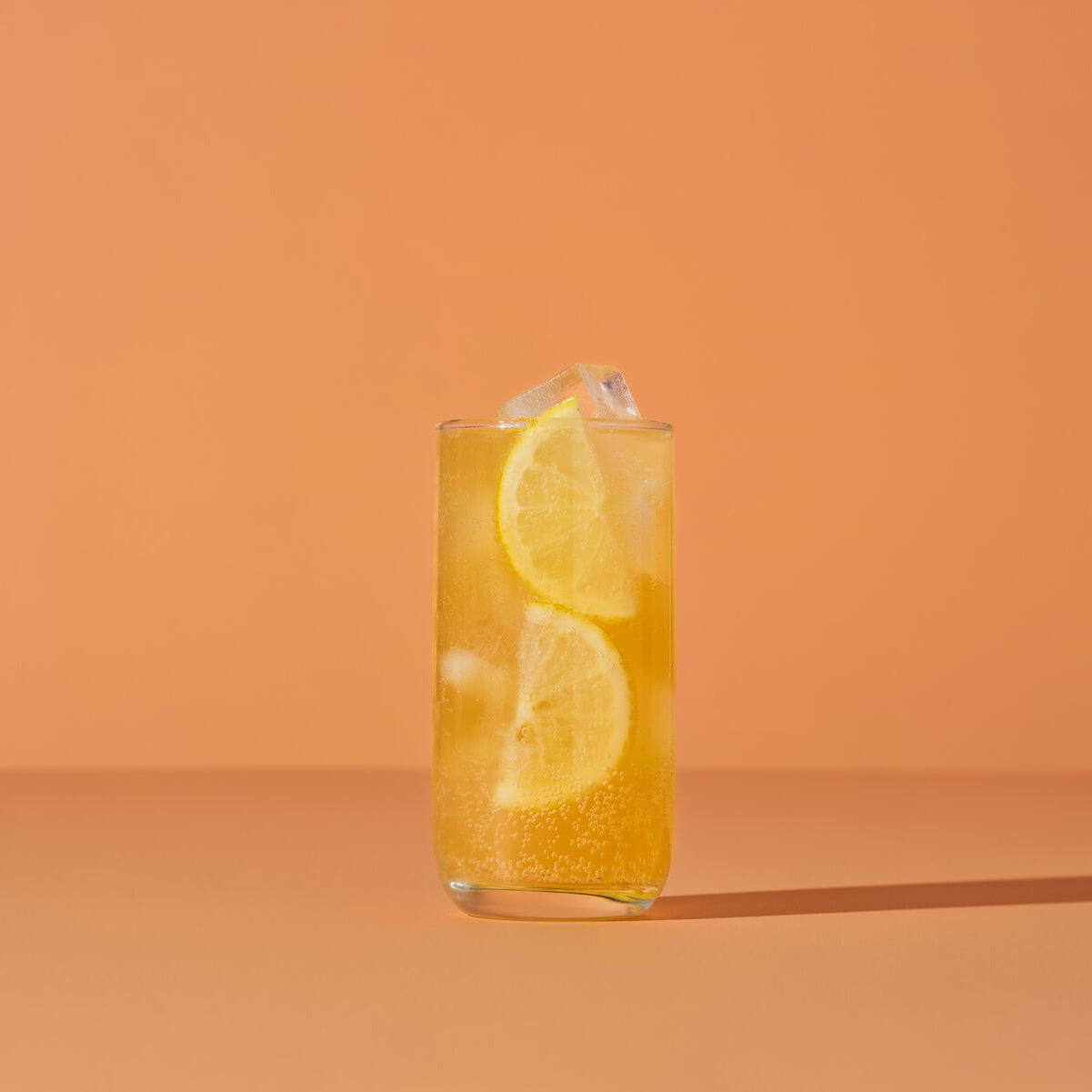Glass of orange juice with lemon slices on an orange background