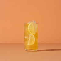 Glass of orange juice with lemon slices on an orange background