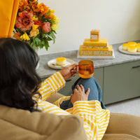 Person in a yellow and white striped shirt sitting on a couch with a cup, with a decorative setting in the background.