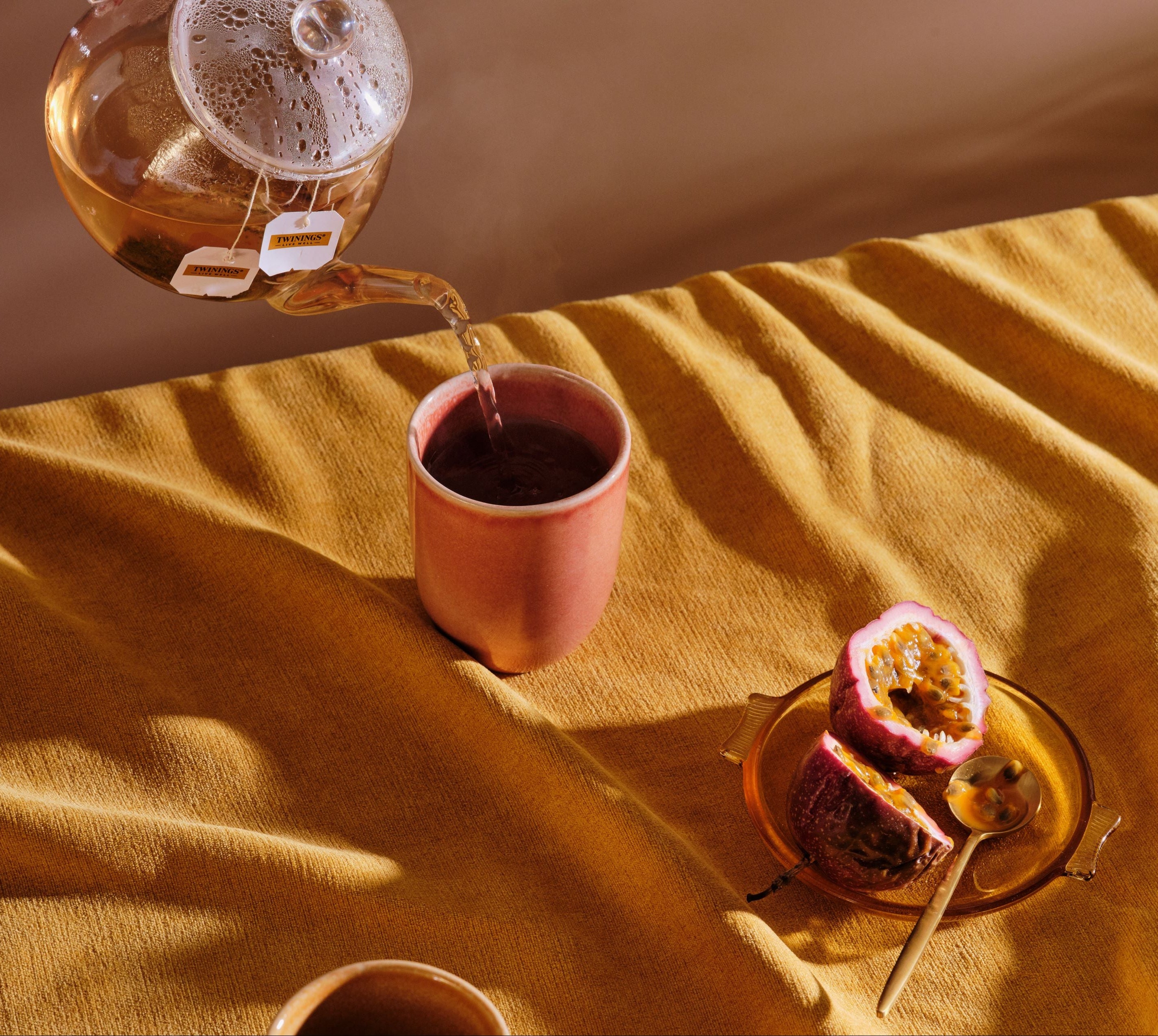 Tea being poured into a pink cup with a sliced passion fruit on a yellow cloth.